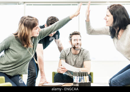 Vier Personen sitzen an einem Tisch, Kollegen bei einer Planung treffen hohe Fiveing einander. Stockfoto