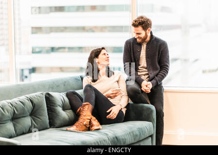 Zwei Personen, auf einem Sofa mit ihren Füßen bis entspannend, saß eine Frau und ein Mann sitzt mit ihr zu reden. Stockfoto