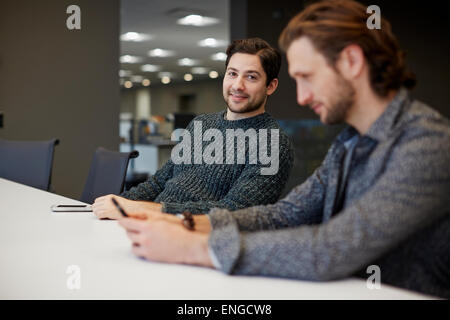 Zwei Männer sitzen an einem Tisch, einer mit seinem Smartphone. Stockfoto