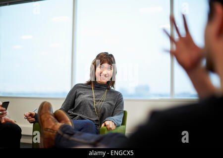 Eine Frau sitzt in einem Büro mit jemandem sprechen, mit den Füßen oben auf den Tisch. Stockfoto