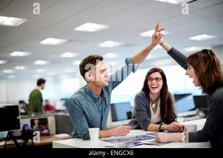 Drei Menschen in einem Büro mit Blick auf Fotografien und eine hohe fünf Geste. Stockfoto