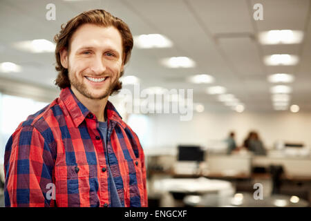 Ein gut aussehender Mann trägt ein kariertes Hemd in einem großen offenen Büro. Stockfoto