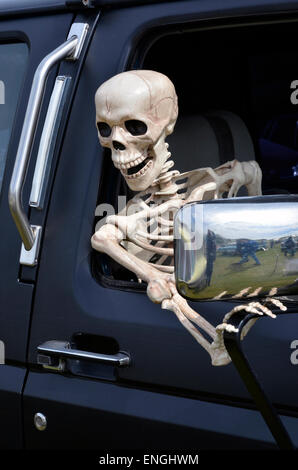 Lange gewartet? Ein Skelett lehnt sich aus dem Fenster eines großen SUV in einem langen Stau stecken oder der Teufel reitet! Stockfoto