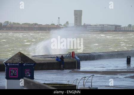 Bei schlechtem Wetter zwei Menschen stehen an der Strandpromenade und beobachten Sie, wie eine große Welle, verursacht durch die raue See Abstürze in der Ufermauer in Southsea, Portsmouth, Hampshire, England. Stockfoto