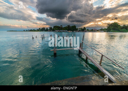 Alten und beschädigten Holzsteg am See Poso in Zentral-Sulawesi, Indonesien, mit dramatischen Wolkengebilde am Horizont bei Sonnenuntergang. Stockfoto