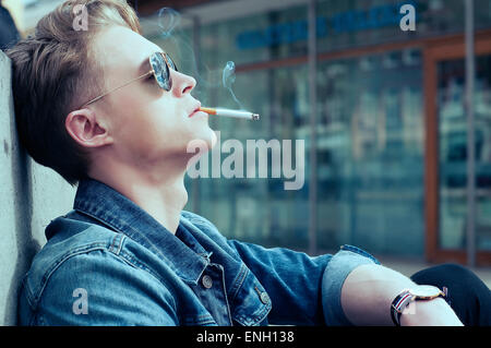 Kaukasischen Jüngling in Jeansjacke und rauchte eine Zigarette in London Sonnenbrillen Stockfoto