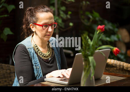 Weibliche Freiberufler mit einem Laptop in einem Sommercafé. Stockfoto