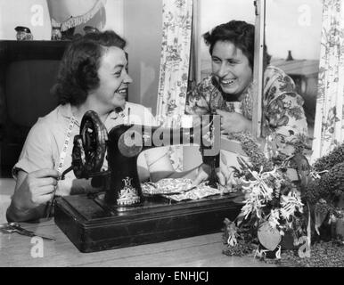 Bei ihrer Nähmaschine beschäftigt ist Frau Beaty Evans, nebenan die Nachbarin, Frau Betty Davies sieht am Fenster, die neueste Badekleidung zu diskutieren. Juli 1955 Stockfoto