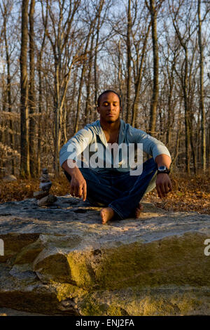 Afrikanische amerikanischer Mann meditiert auf einem Felsen im Wald Stockfoto