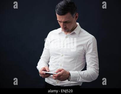 Ernst Kaufmann mit Smartphone über schwarzen Hintergrund. Tragen im weißen Hemd Stockfoto