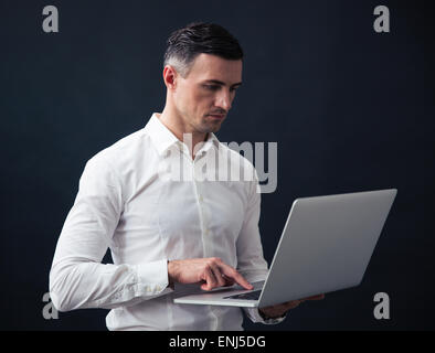 Ernst Kaufmann stehend und mit Laptop auf schwarzem Hintergrund Stockfoto