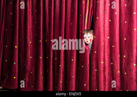 Lustige kleine Junge im Make-up für seine Schauspielerei Cue stossen seinen Kopf zwischen den Vorhängen, wie er wartet auf seinen Auftritt zu warten Stockfoto
