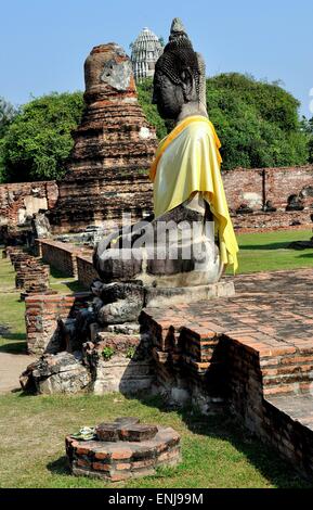 Ayutthaya, Thailand: Große Stein Buddha-Statue in einer gelben Schärpe Seide gehüllt sitzt inmitten der Ruinen am Royal Wat Mahathat Stockfoto