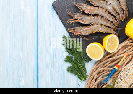 Frische rohe Riesengarnelen und Ausrüstung für die Fischerei auf Holztisch. Draufsicht mit Textfreiraum Stockfoto