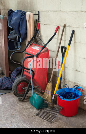Schubkarre und andere Tools in einem Reitsport Stallhof. Eimer, Bürsten, Teppiche und Ausmisten Gabel. Stockfoto