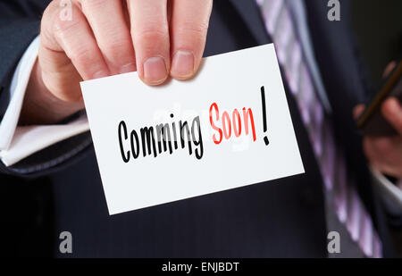 Ein Geschäftsmann hält eine Visitenkarte mit den Worten: Coming Soon, darauf geschrieben. Stockfoto