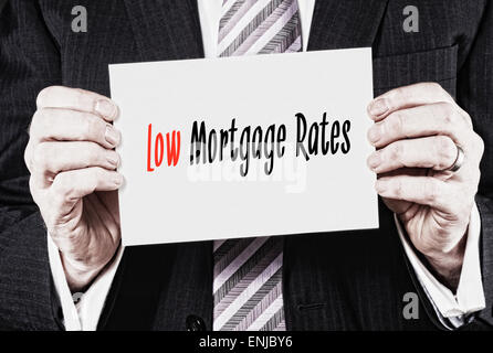 Ein Geschäftsmann hält eine Visitenkarte mit den Worten, niedrige Hypothekenzinsen, darauf geschrieben. Stockfoto