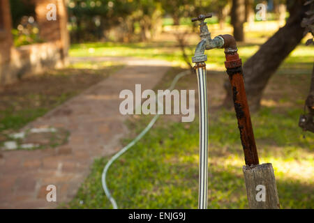 Alte rostige Wasser Armatur mit Schlauch im Garten Stockfoto