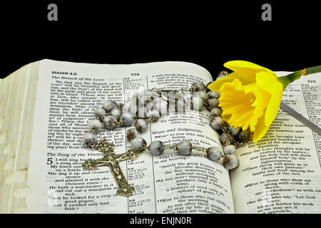 Nahaufnahme eines Jahrgangs Jobs Tränen bead Rosenkranz und Kruzifix mit einer Narzisse Blüte auf eine Bibel öffnen um Isiah auf schwarzem Hintergrund Stockfoto