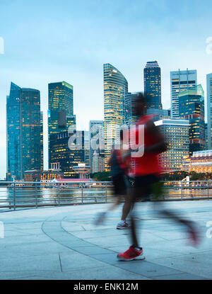 Menschen laufen in der Dämmerung auf Singapur-Damm. Singapur Downtown Core im Hintergrund Stockfoto