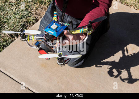 Ein Mann kniet auf einem Bürgersteig und hält seine DIY Projekt Quad Copter Drohne. Stockfoto