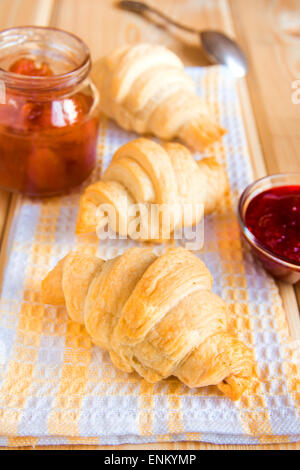 Hausgemachte frische Croissants mit Marmelade (Marmelade) auf Serviette und Holztisch Stockfoto