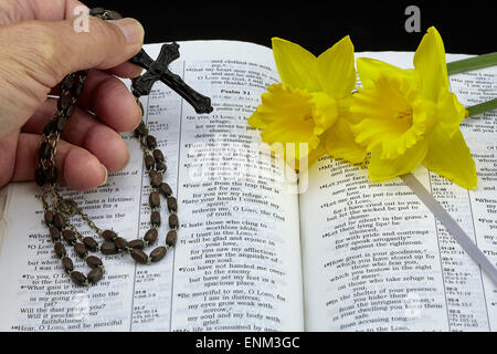 Mann hält Vintage Rosenkranz mit Kreuz mit Bibel und Blumen Stockfoto