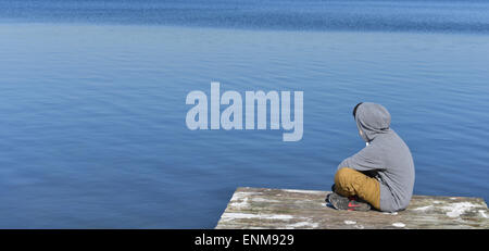 Kleiner Junge sitzt auf eine geworfene Seenlandschaft mit Steg am See Stockfoto