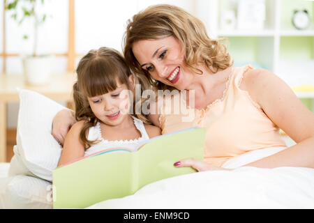 Glückliche Mutter und Tochter lesen ein Buch zusammen im Bett Stockfoto