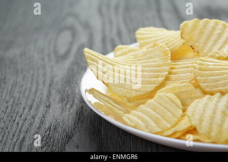 geriffelte Kartoffelchips in weißer Teller auf Holztisch Stockfoto