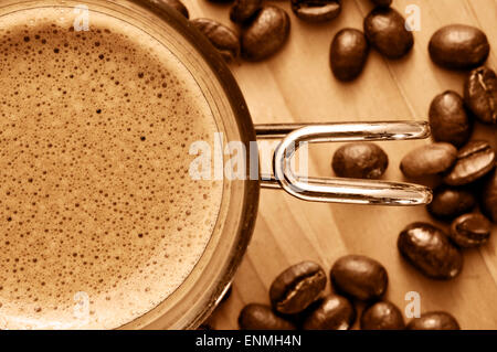 Nahaufnahme von einer Tasse Kaffee und einige Kaffeebohnen auf einem Holztisch in Sepia Tönung Stockfoto