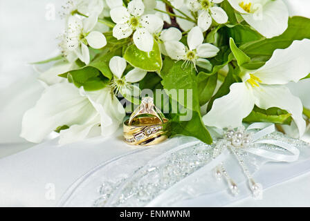 Trauringe mit Trillium Brautstrauß auf einem weißen satin Kissen. Stockfoto