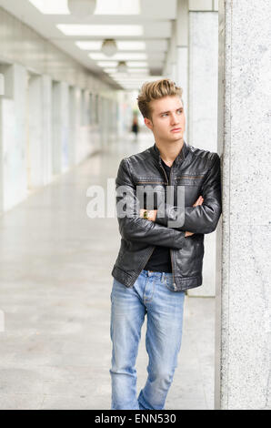 Attraktive blonde junge Mann mit Lederjacke draußen gegen Pfeiler, wegschauen Stockfoto