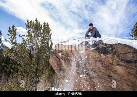 Männliche Bergsteiger reinigt Schnee von oben auf einen Felsblock in Rocky Mountain Nationalpark, Colorado Stockfoto