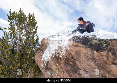 Männliche Bergsteiger reinigt Schnee aus der Spitze von einem Felsbrocken in Rocky Mountain Nationalpark, Colorado Stockfoto