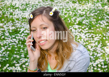 Brünette sitzt unter dem Gänseblümchen im Frühjahr mit ihrem smartphone Stockfoto