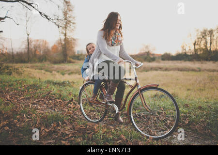 Eine Mutter-eine altmodische Fahrrad Pedale während ihrer Tochte auf dem Rücken reitet. Stockfoto