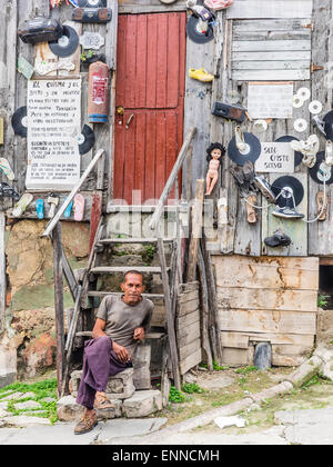 Ein Hispanic kubanischen sitzt Man auf den Stufen von seinem sehr seltsam, eingerichtete unkonventionell Holzhaus. Stockfoto