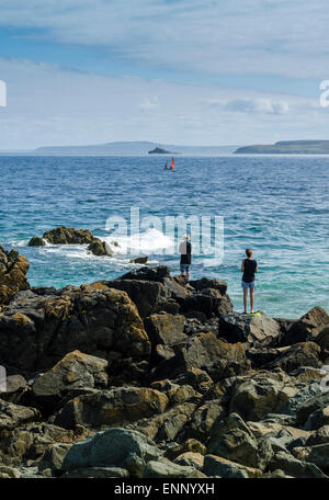 Ein paar Blick über das Meer in St Ives Bay, Cornwall. Ein Segelboot auf dem Horizont und Godrevy Leuchtturm in der Ferne. Stockfoto