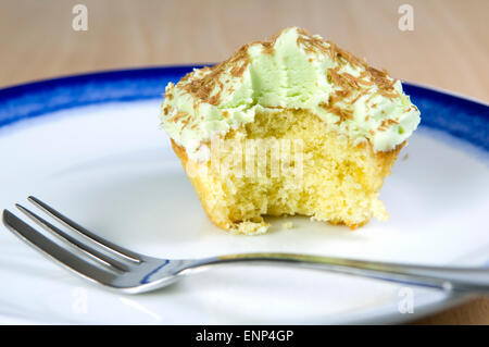 Pistazien Cupcake mit grünen Zuckerguss, Schokolade Späne und einen Bissen genommen, der auf einem weißen und blauen Teller Stockfoto