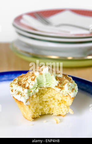 Pistazien Cupcake mit grünen Zuckerguss, Schokolade Späne und einen Bissen genommen, der auf einem weißen und blauen Teller Stockfoto