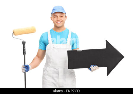 Junge männliche Dekorateur in einer weißen Uniform mit einem Farbroller und einem großen schwarzen Pfeil Recht isoliert auf weißem Hintergrund Stockfoto