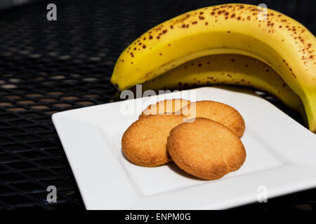 Gesunder Snack leckere Butterplätzchen und reife Bananen.  Vier Cookies auf weißen Teller vor frisches Obst. Stockfoto