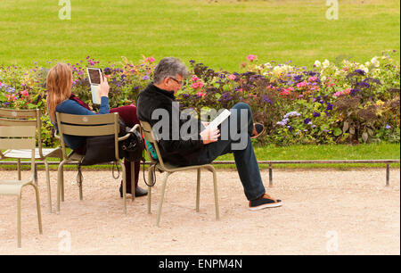 Paar-Lesung mit ihren Tabletten, Entspannung im Jardin du Luxembourg. Stockfoto