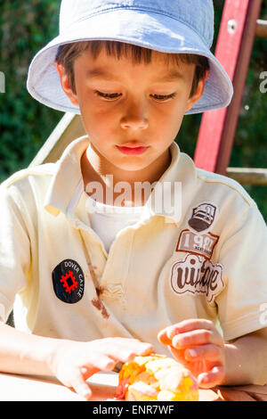 Halbe Länge Aufnahme eines kaukasischen Kindes, Junge, 8-9 Jahre alt, im Freien stehend mit einem Floppy Sonnenhut spielen mit Spielteig auf einem Holztisch. Stockfoto