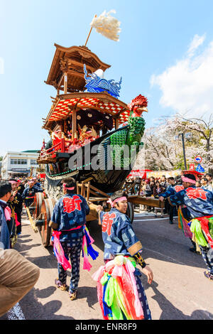 Ein Team von Männern, die sich bemühen, einen massiven Dashi, Yama, Holzwagen zu schieben, umgeben von Massen von Touristen, die das Frühlingsfest von Inuyama beobachten Stockfoto