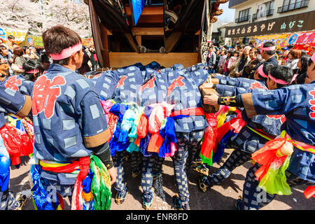 Ein Team von Männern, die sich bemühen, einen massiven Dashi, Yama, Holzwagen zu schieben, umgeben von Massen von Touristen, die das Frühlingsfest von Inuyama beobachten Stockfoto