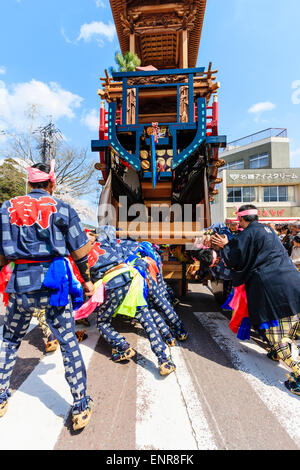 Ein Team von Männern, die sich bemühen, einen massiven Dashi, Yama, Holzwagen zu schieben, umgeben von Massen von Touristen, die das Frühlingsfest von Inuyama beobachten Stockfoto