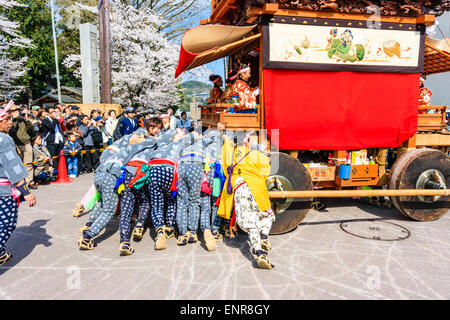 Ein Team von Männern, die sich bemühen, einen massiven Dashi, Yama, Holzwagen zu schieben, umgeben von Massen von Touristen, die das Frühlingsfest von Inuyama beobachten Stockfoto