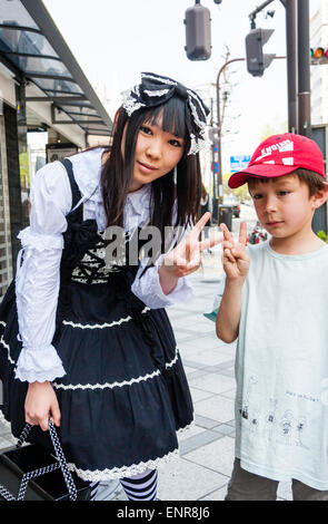 Japan, Kyoto. Kostüm spielen Mädchen, Gothic Lolita viktorianischen Maid schwarzen Outfit. Posieren mit Asian-Western gemischten Rennen Kind. Beide geben Frieden Geste. Stockfoto